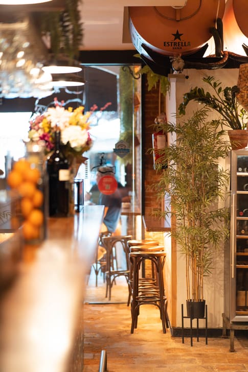 La barra de L'Aixeta Sitges, con flores frescas y la luz de la calle al fondo